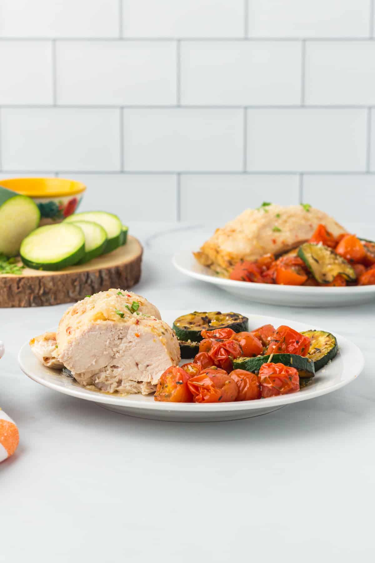 baked Italian chicken breast with a bite taken showing the texture on a white plate with roasted vegetables