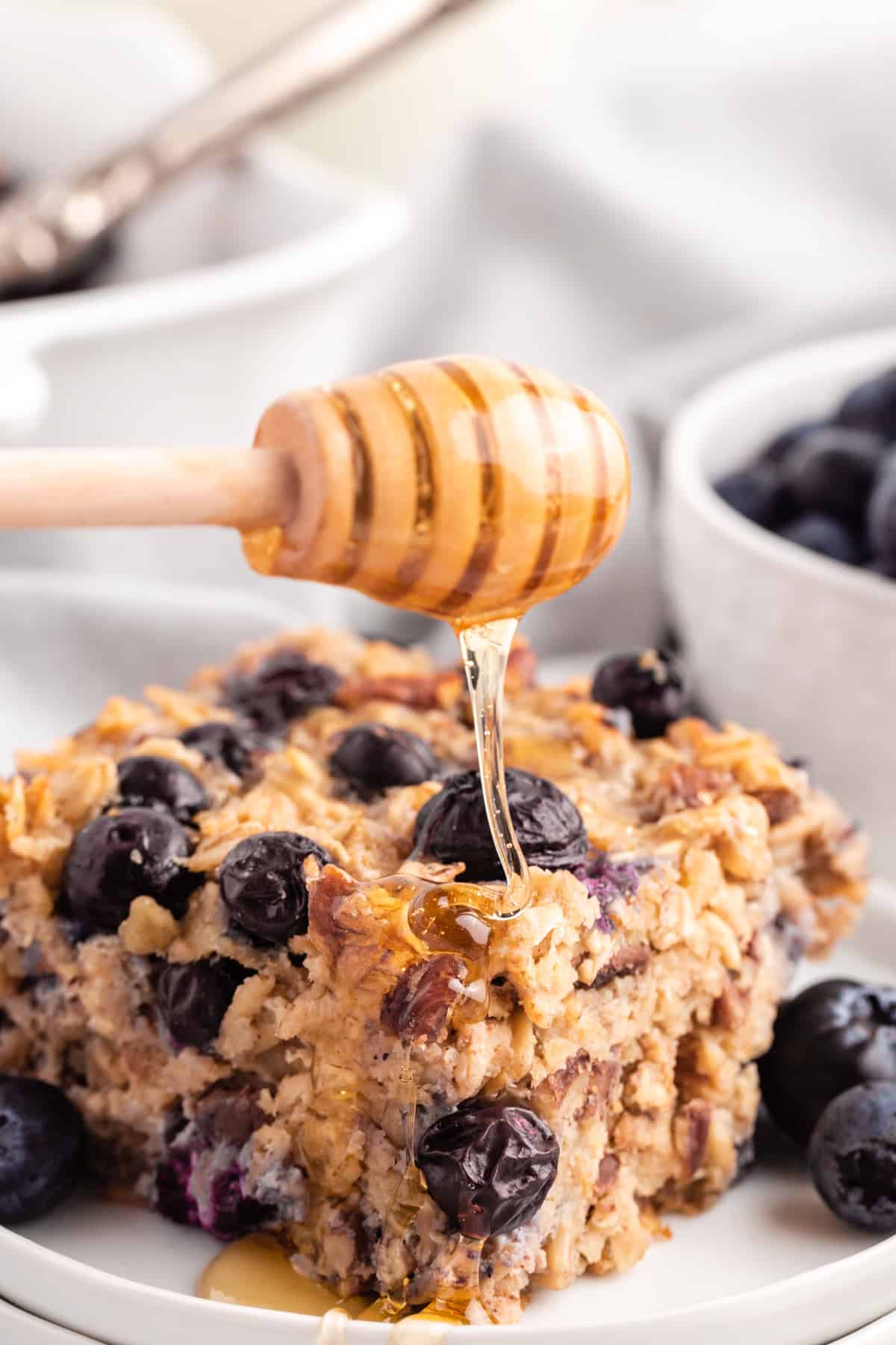 drizzling honey onto a piece of blueberry baked oatmeal on a white plate