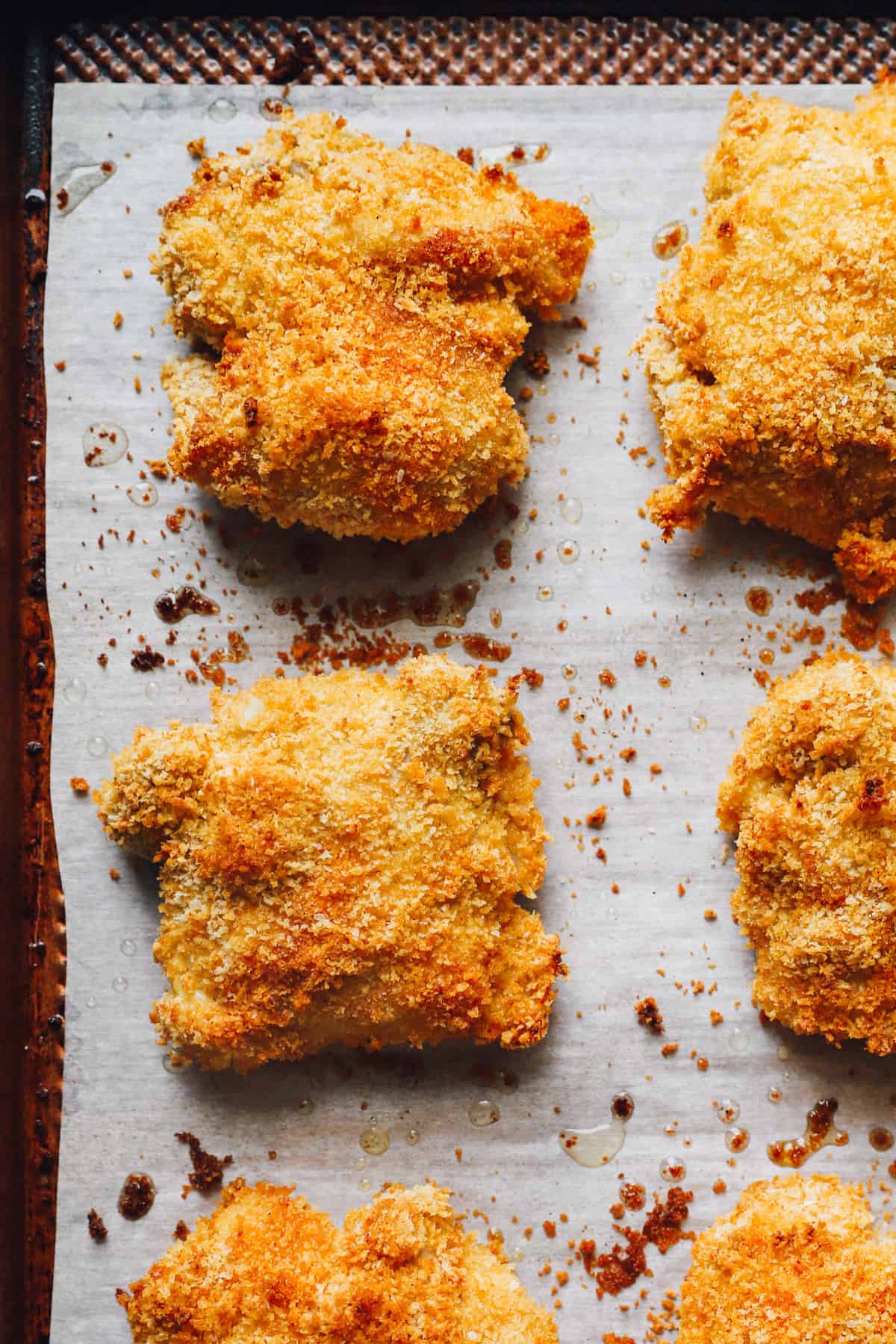 chicken thighs coated in breadcrumbs, on a parchment paper lined baking sheet after baking.