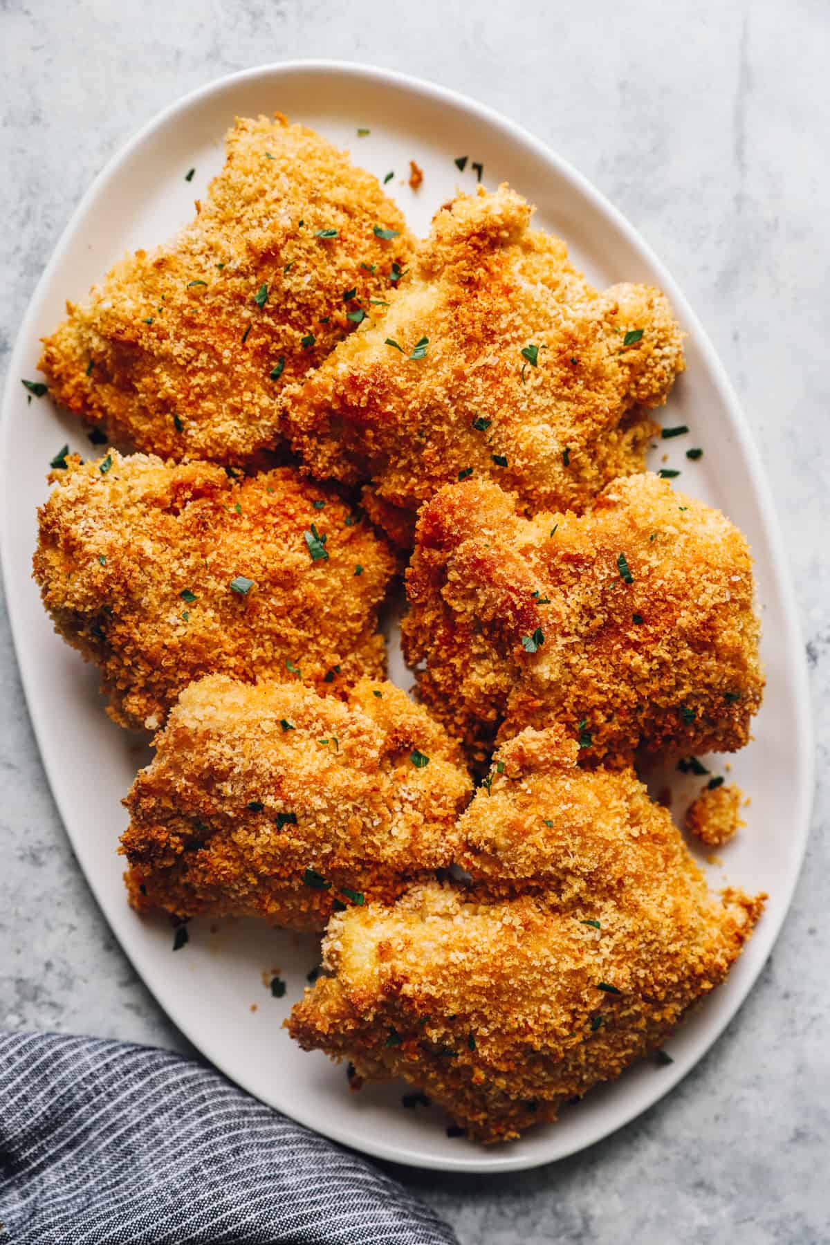 crispy baked and breaded chicken thighs on a white serving plate.