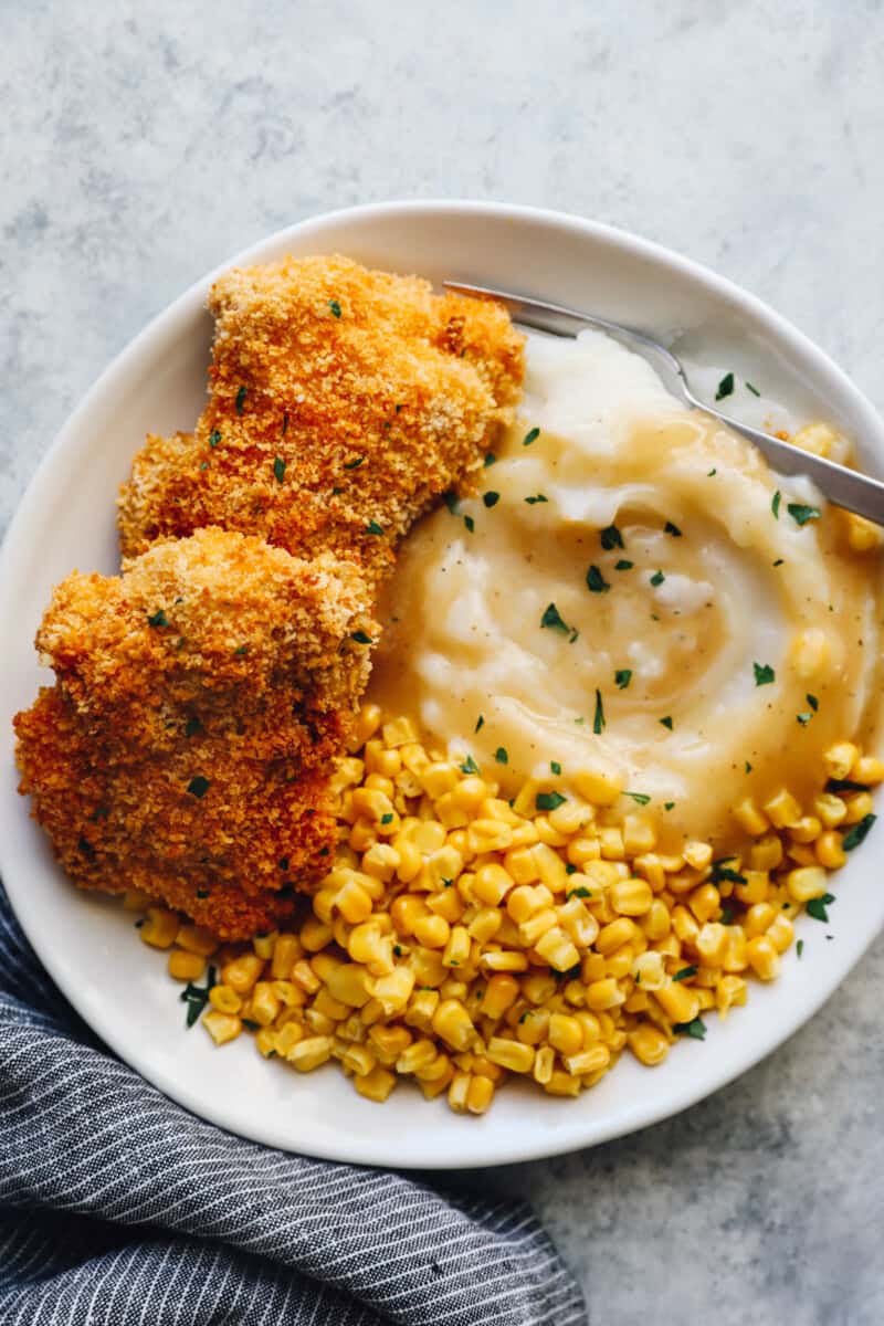 baked chicken thighs on a white plate with mashed potatoes and corn with a fork