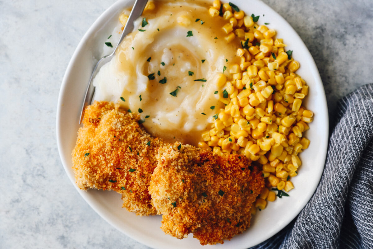baked chicken thighs on a white plate with mashed potatoes and corn with a fork