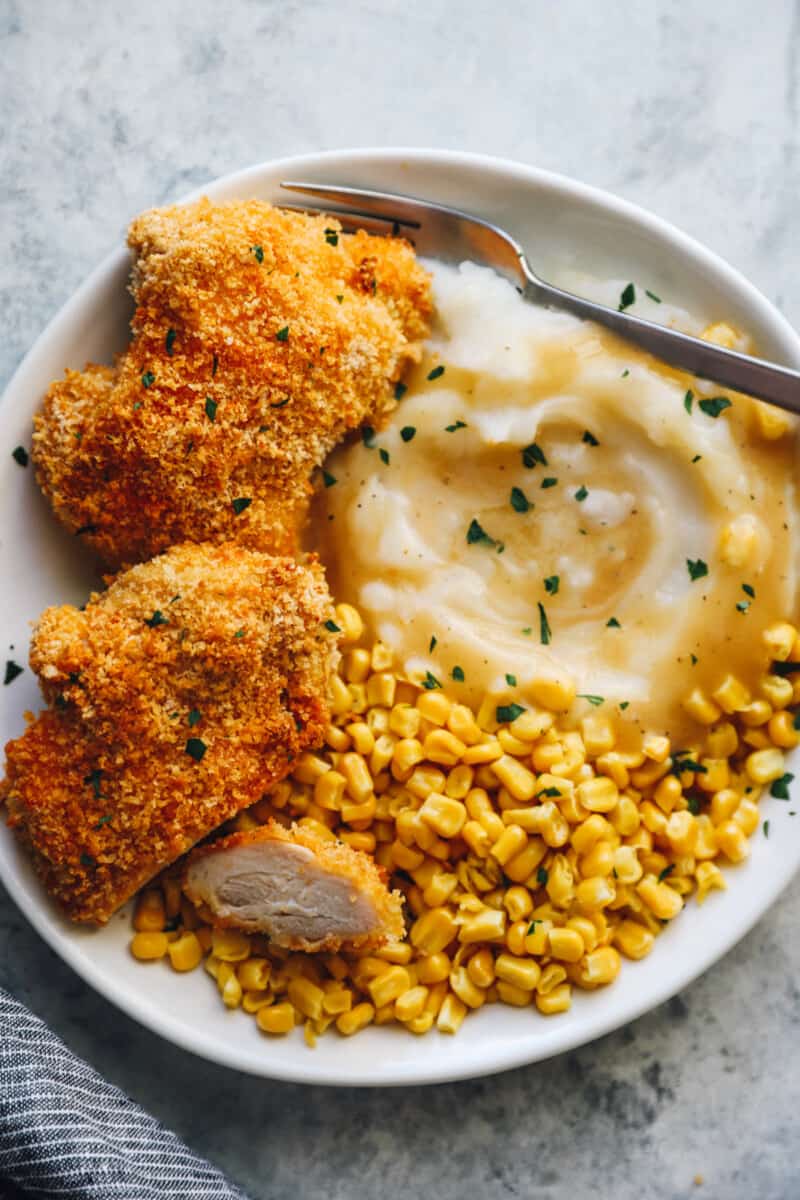 baked chicken thighs on a white plate with mashed potatoes and corn with a fork
