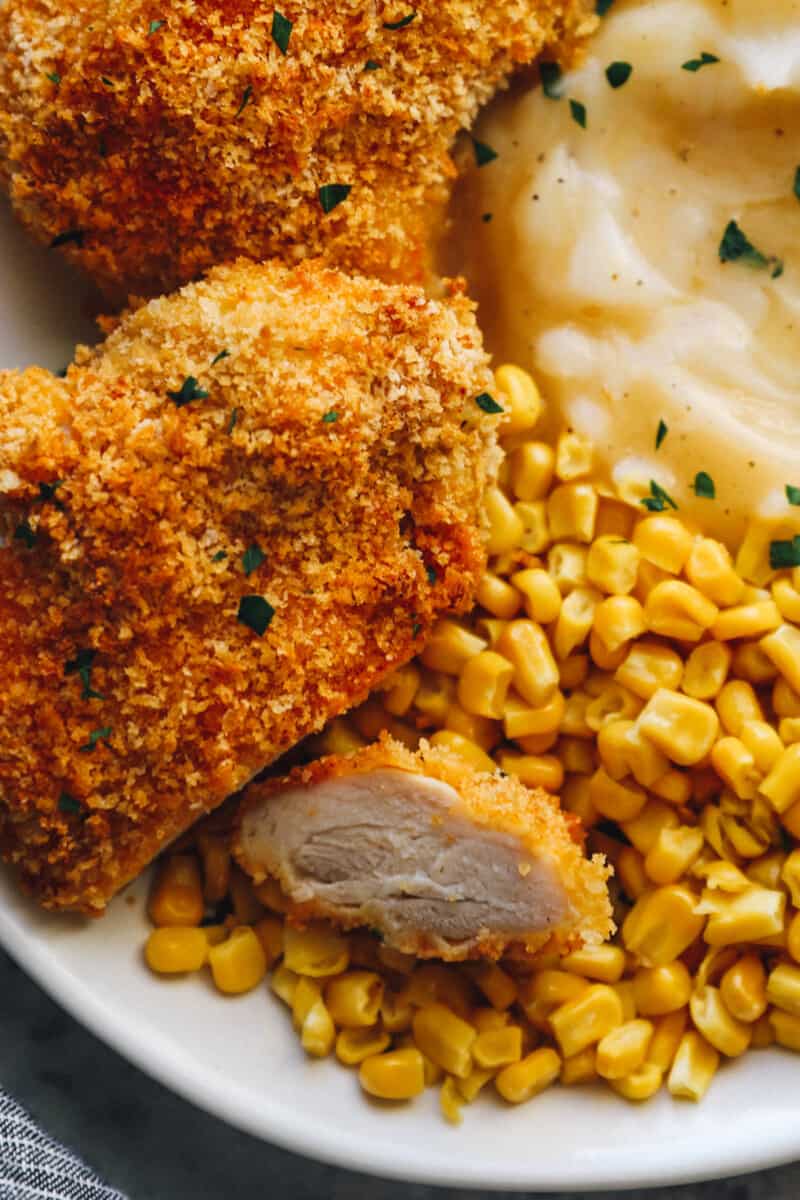 baked chicken thighs on a white plate with mashed potatoes and corn