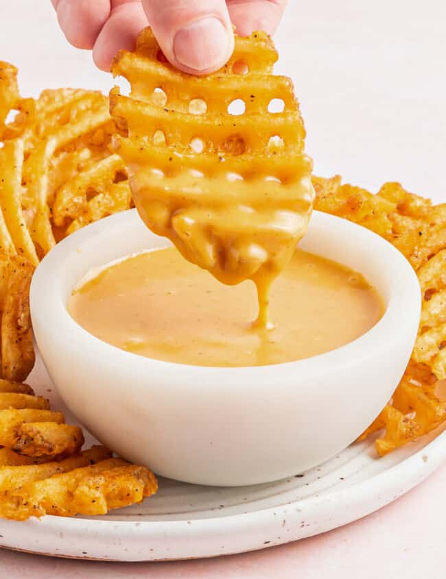 hand dipping a waffle fry into a bowl of chick-fil-a sauce