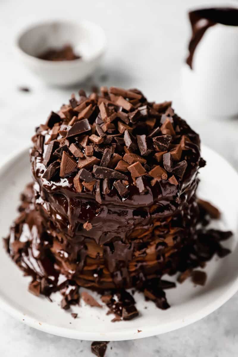 stack of chocolate pancakes topped with chocolate sauce and chopped chocolate on a white plate