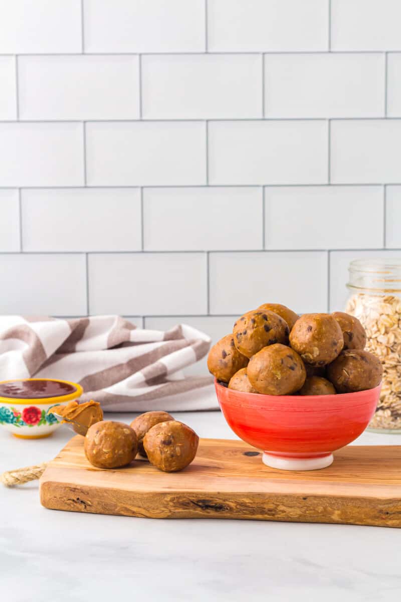 A red bowl full of protein balls on a wood serving board.