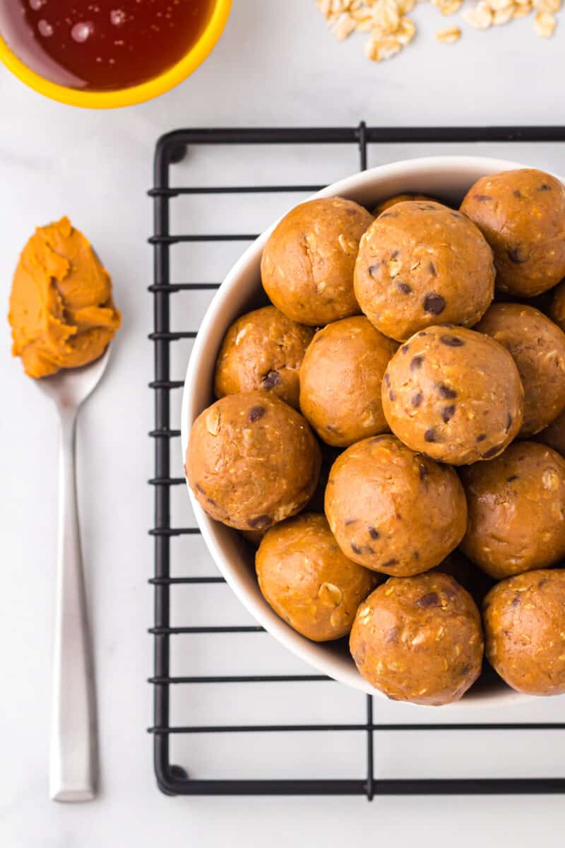 Overhead image of freshly made chocolate peanut butter protein balls in a white bowl and a spoon filled with peanut butter next to it.