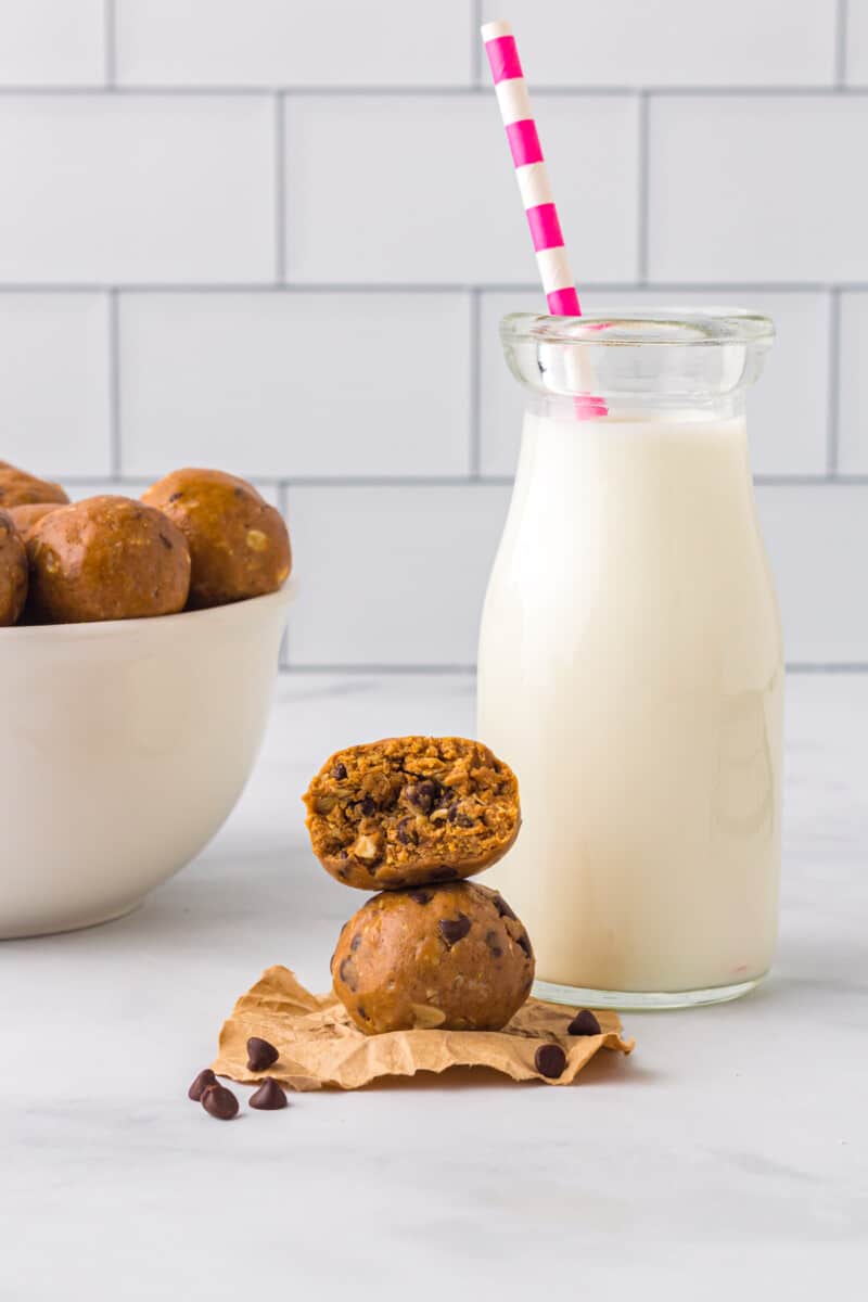 stack of 2 chocolate peanut butter protein balls with a bite taken from the top one with a glass of milk