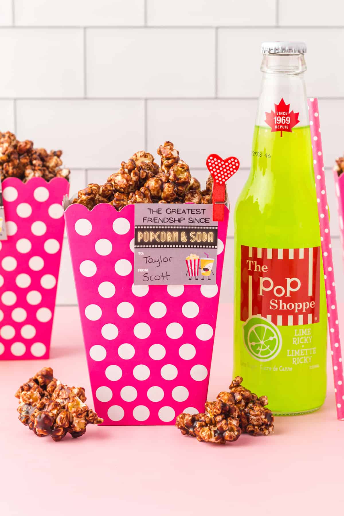 chocolate popcorn in a pink and white popcorn container next to a lime bottle of soda