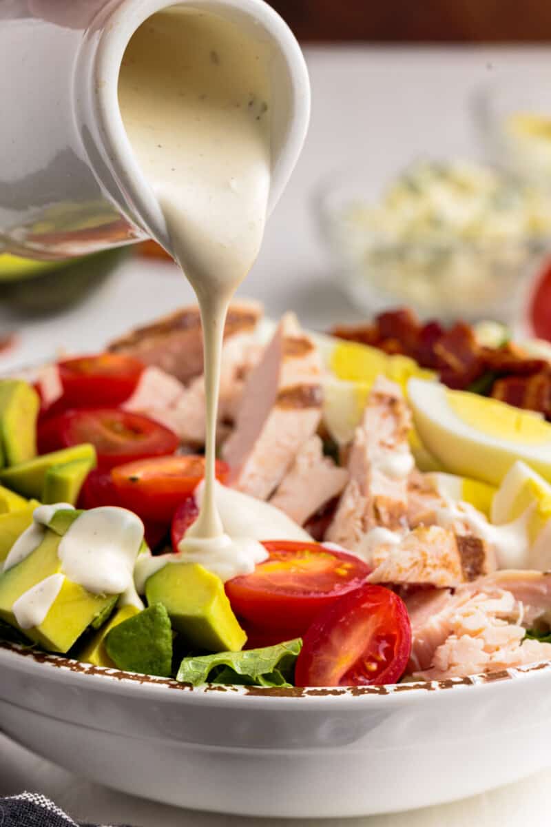 pouring dressing onto cobb salad in a bowl