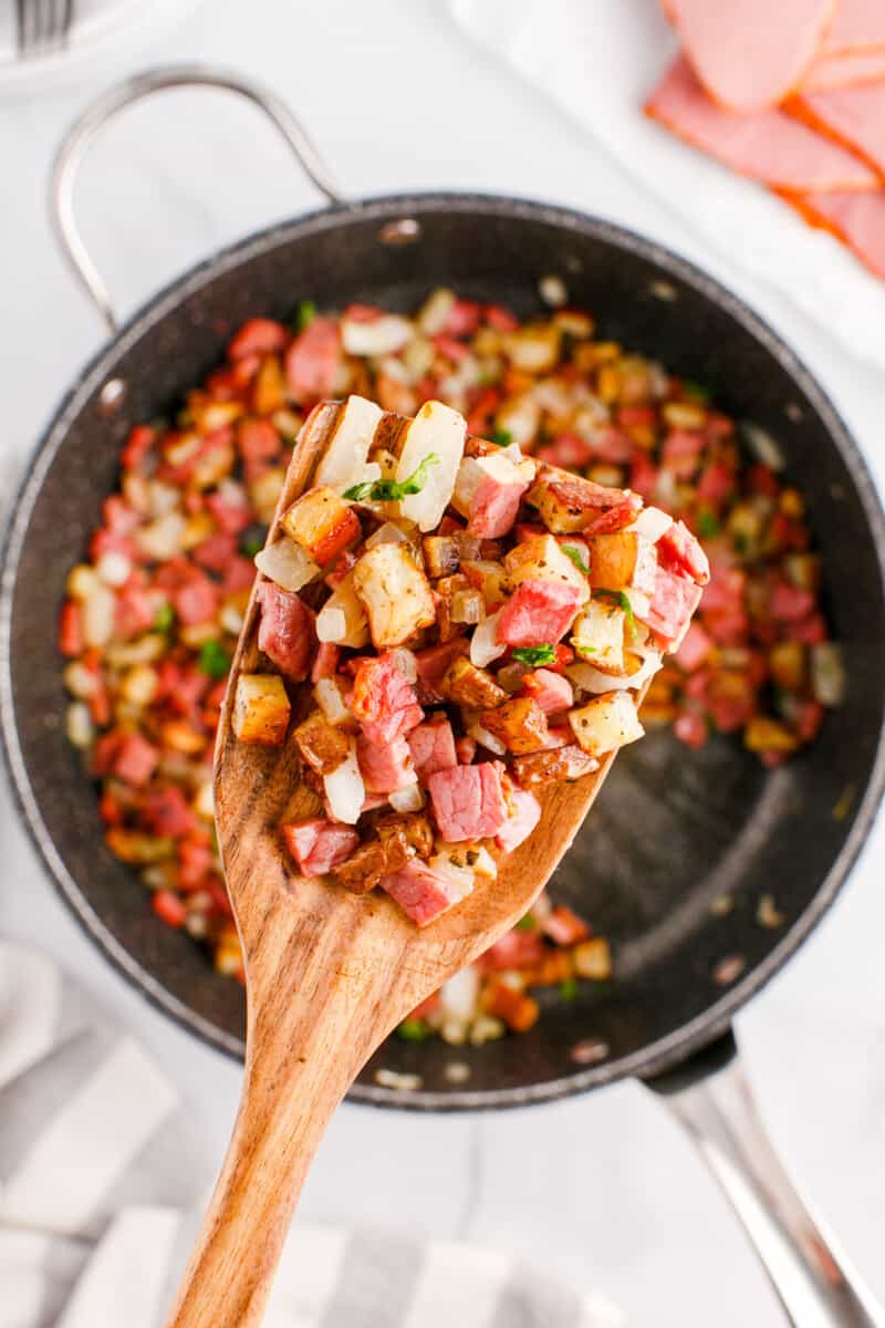 corned beef and potato hash on a wood spoon above a skillet