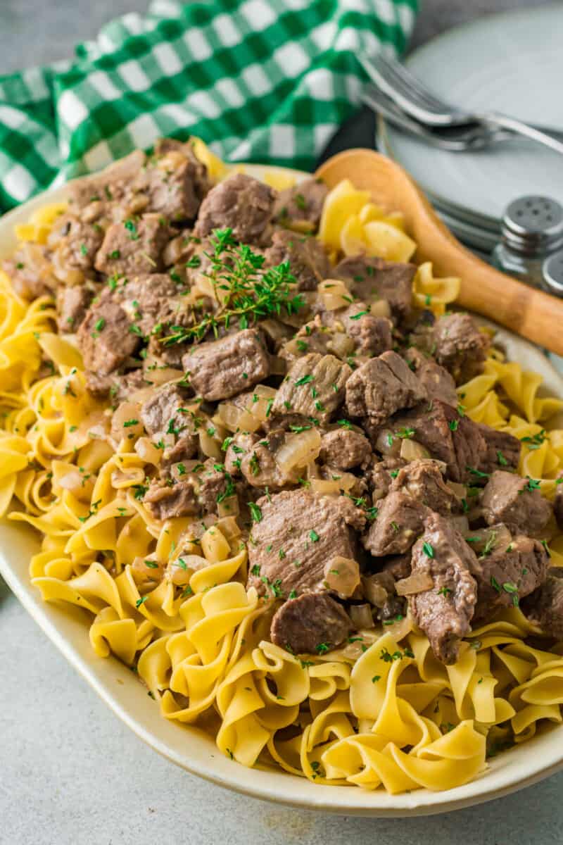 beef and noodles on a white serving platter with a wood spoon