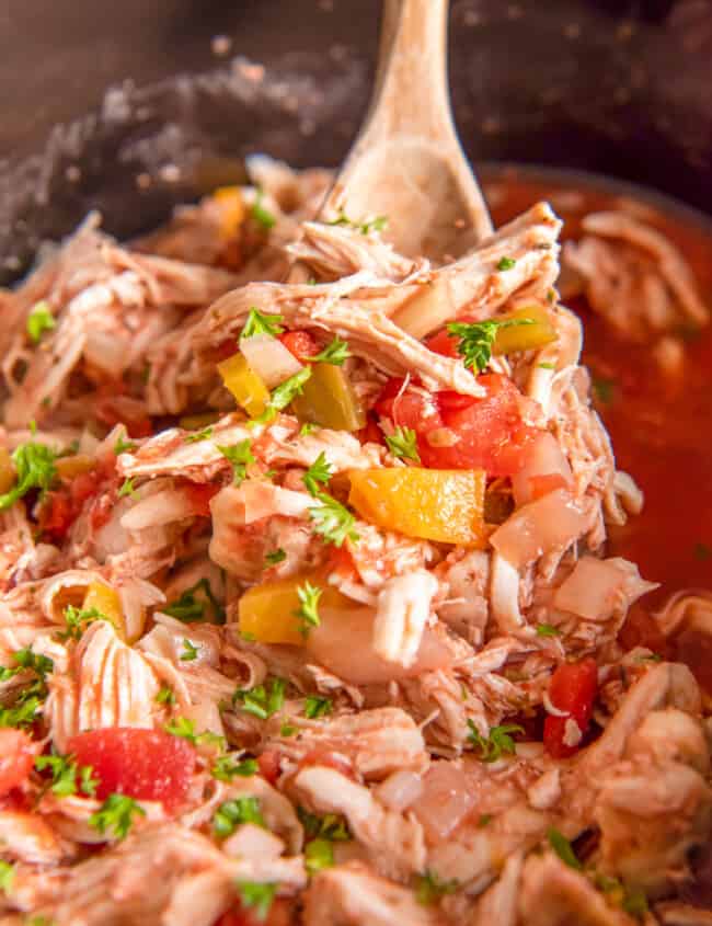 shredded italian chicken in a crockpot with a wood spoon