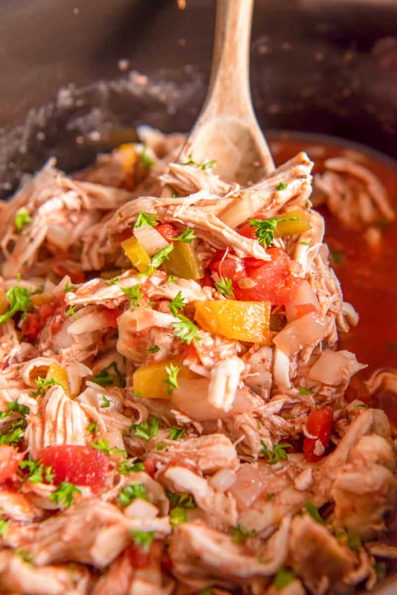 shredded italian chicken in a crockpot with a wood spoon