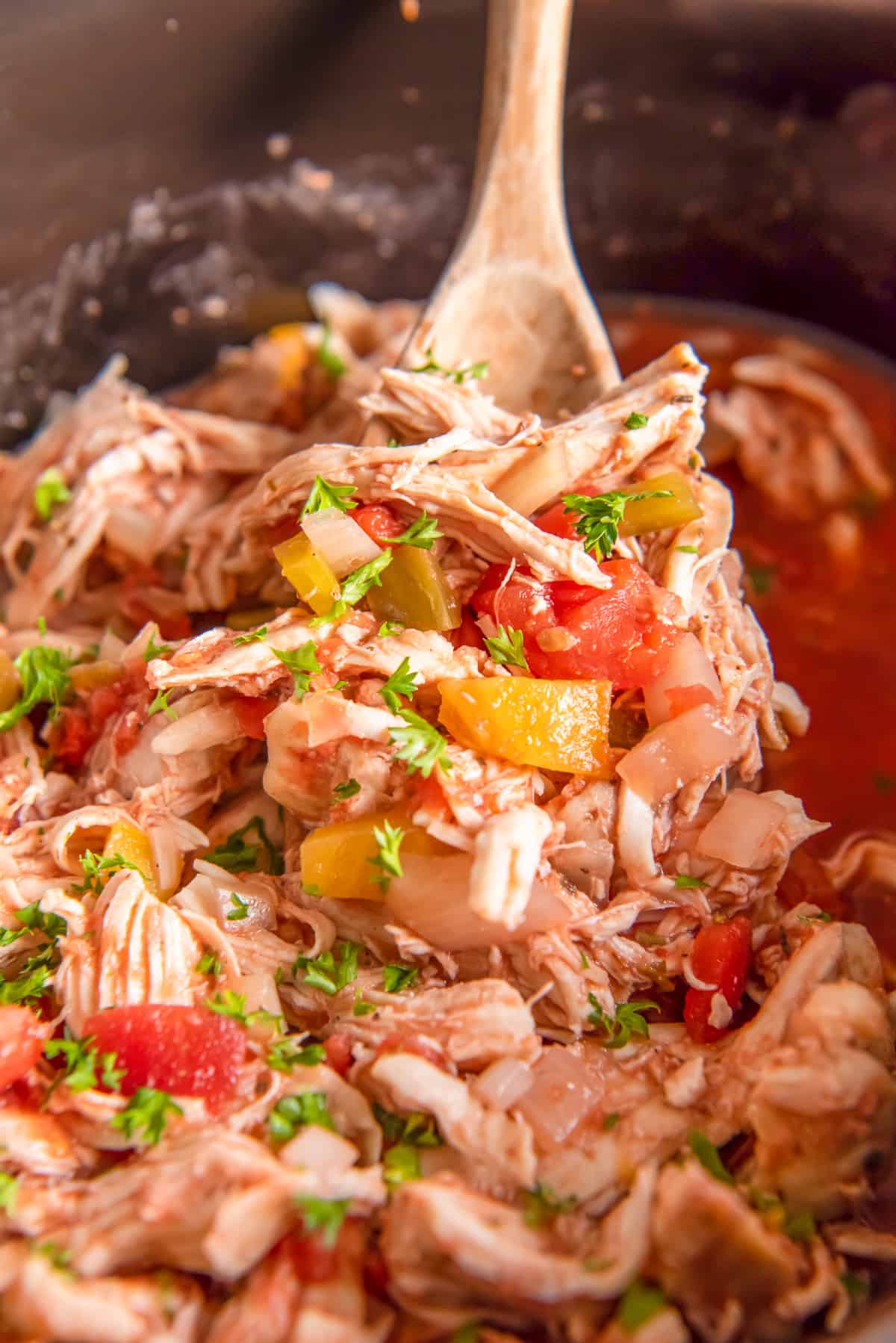 shredded italian chicken in a crockpot with a wood spoon