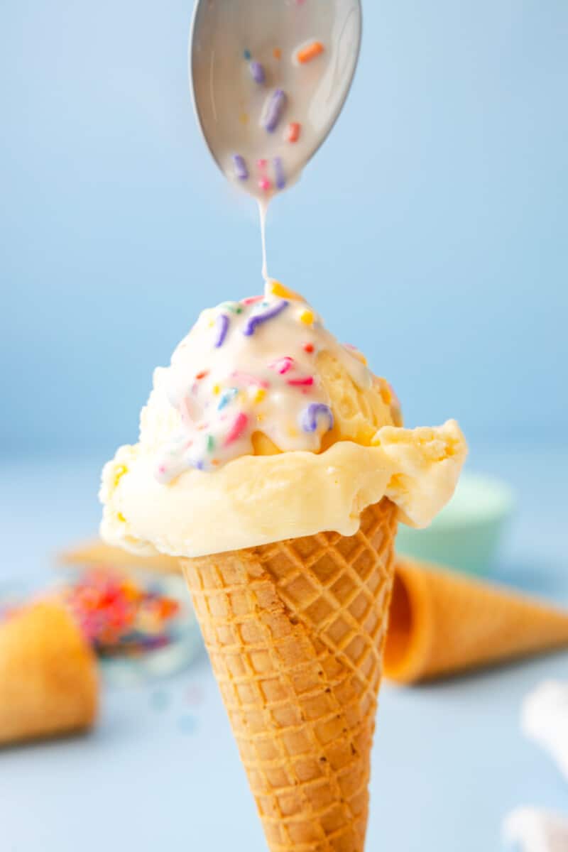 spoon adding funfetti magic shell to a vanilla ice cream cone