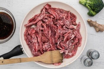 sliced flank steak in a skillet with a wood spoon