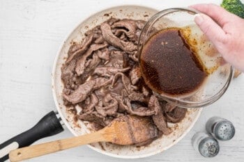 pouring sauce onto steak in a skillet with a wood spoon