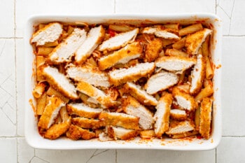 chicken strips on top of noodles and sauce in a white baking dish