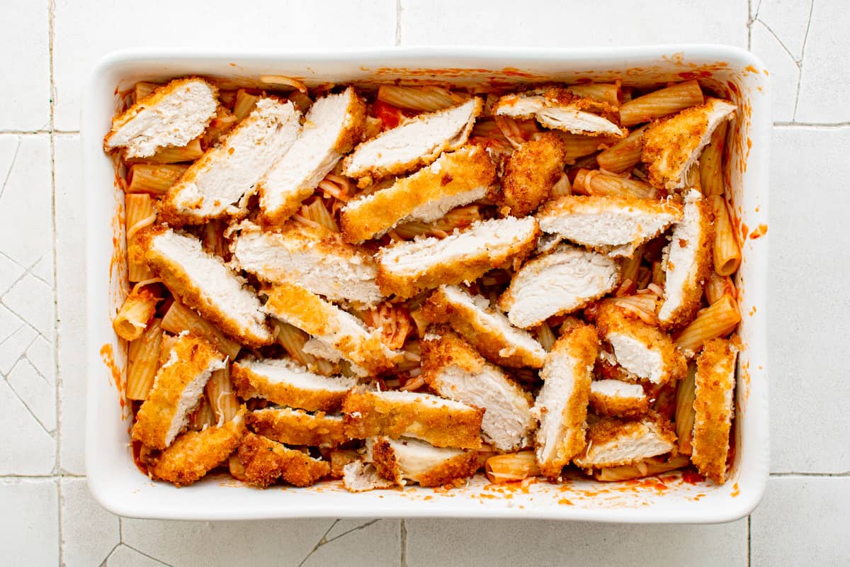 chicken strips on top of noodles and sauce in a white baking dish