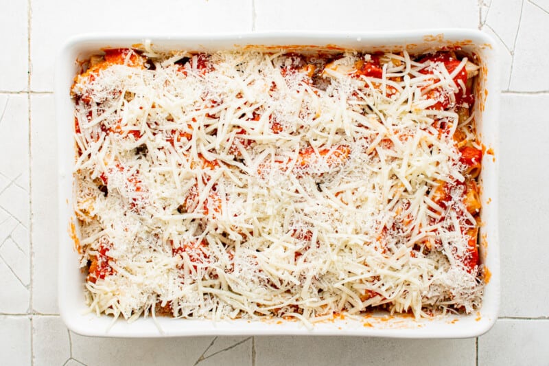 shredded cheese on top of noodles, sauce, and chicken in a white baking dish
