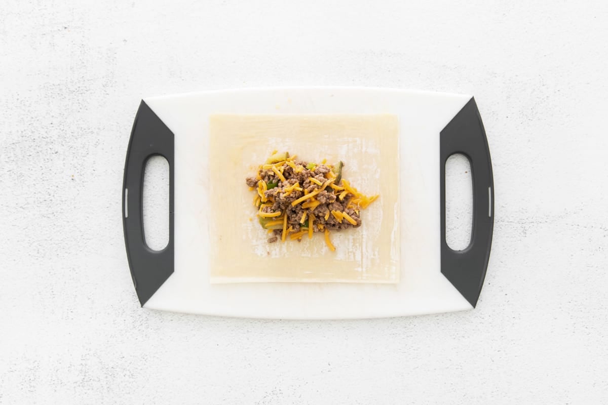 ground beef and cheese on pastry on a cutting board.