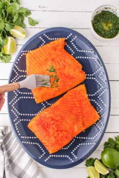 spreading cilantro lime mixture onto salmon fillets on a blue plate