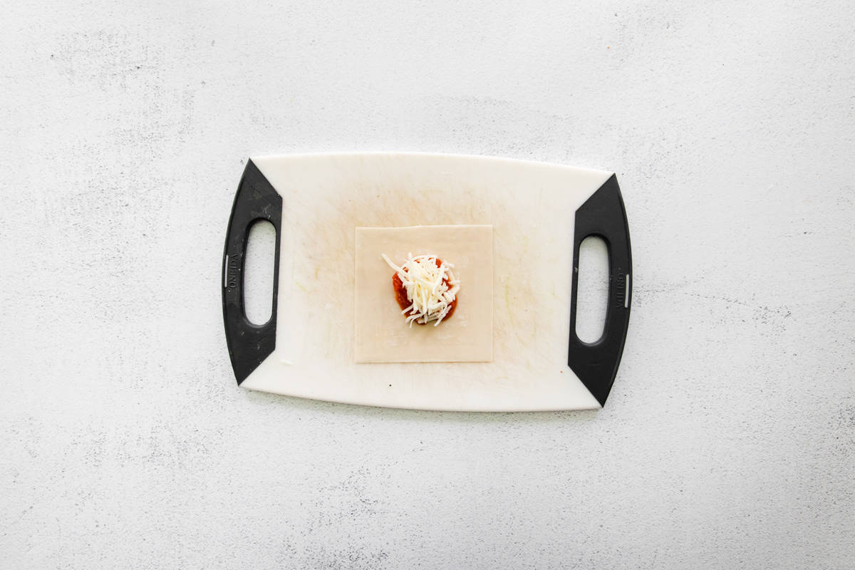 Assembling pizza roll on a white cutting board.