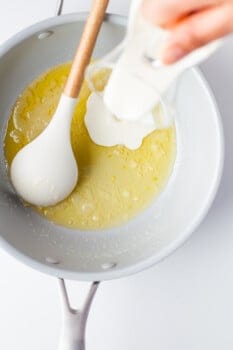 pouring cream into melted butter and garlic mixture in a saucepan with a spoon