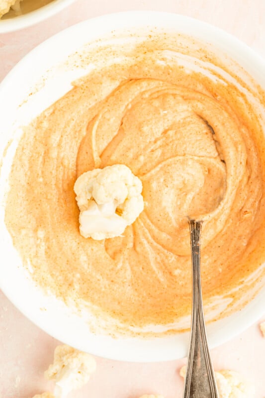 cauliflower floret in a bowl of buffalo batter