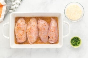 4 chicken breasts topped with Italian dressing in a white baking pan