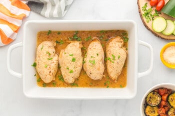 4 chicken breasts topped with Italian dressing in a white baking dish after baking