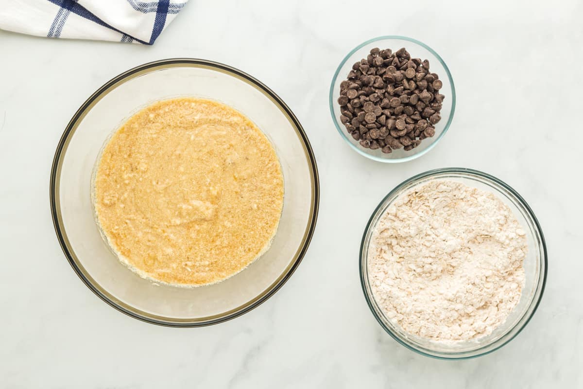 wet and dry ingredients in glass bowls next to a bowl of chocolate chips.