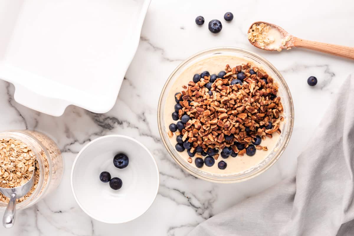 Nuts and blueberries added to oatmeal mixture in a glass bowl. - 10