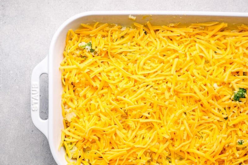 shredded cheddar cheese on top of broccoli rice casserole in a white baking dish