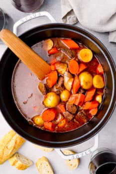 overhead image of beef stew in a Dutch oven with a wood spoon