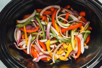 sliced bell peppers and sliced onions in a crockpot before cooking