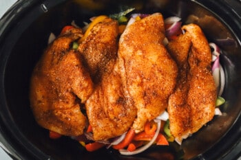 chicken breasts, sliced bell peppers, and sliced onions in a crockpot before cooking