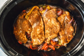 chicken breasts, sliced bell peppers, and sliced onions in a crockpot after cooking