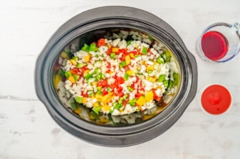 onion, bell pepper, tomatoes, and garlic on top of chicken breasts in a crockpot