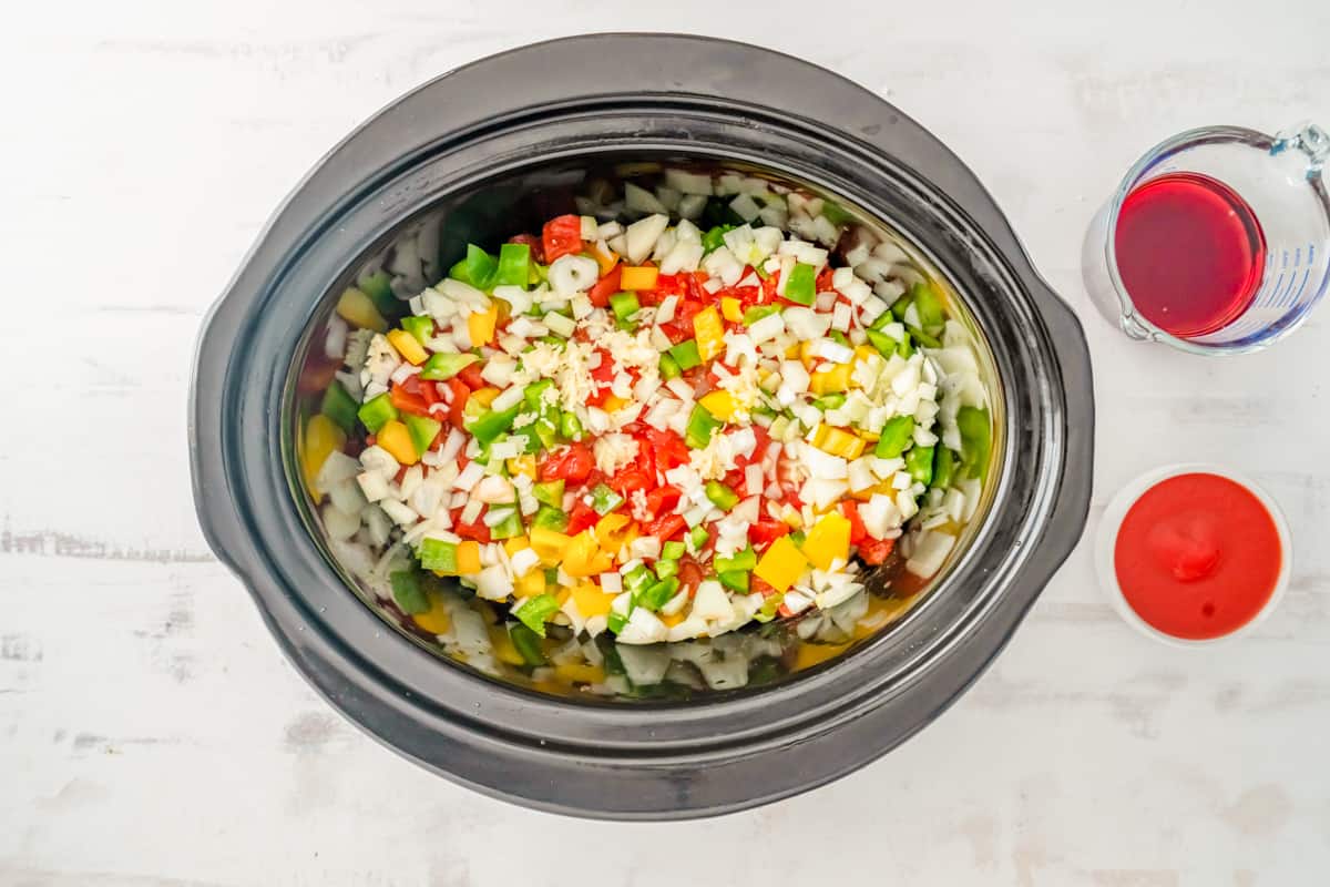 onion, bell pepper, tomatoes, and garlic on top of chicken breasts in a crockpot