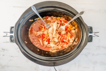 2 forks in a crockpot shredding cooked chicken