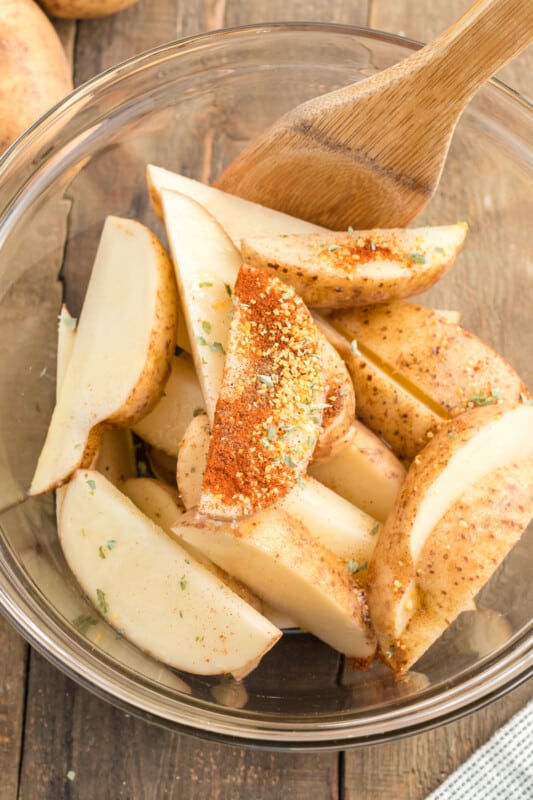 mixing spices into potato wedges in a glass bowl with a wood spoon