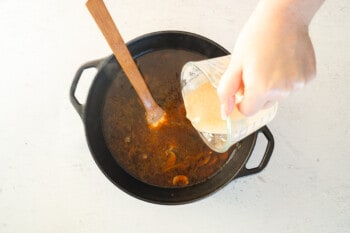 pouring sour cream mixture into beef stroganoff soup in a pot with a wood spoon