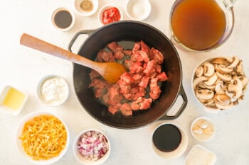 browning stew meat for beef stroganoff soup in a pot with a wood spoon