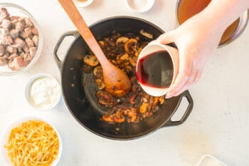 pouring red wine into a pot of onions and mushrooms with a wood spoon