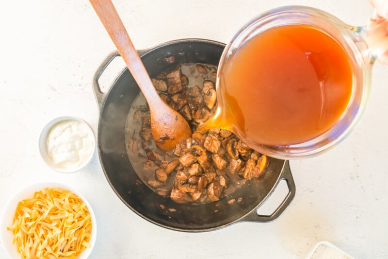 pouring beef stock into pot with a wood spoon