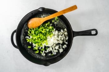 chopped bell pepper and onion in a skillet with a wood spoon