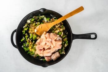 chicken pieces added to sautéed vegetables in a skillet with a wood spoon